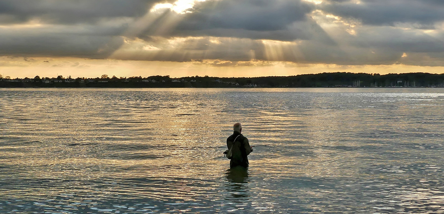 Lystfisker nyder solnedgangen i Strib
