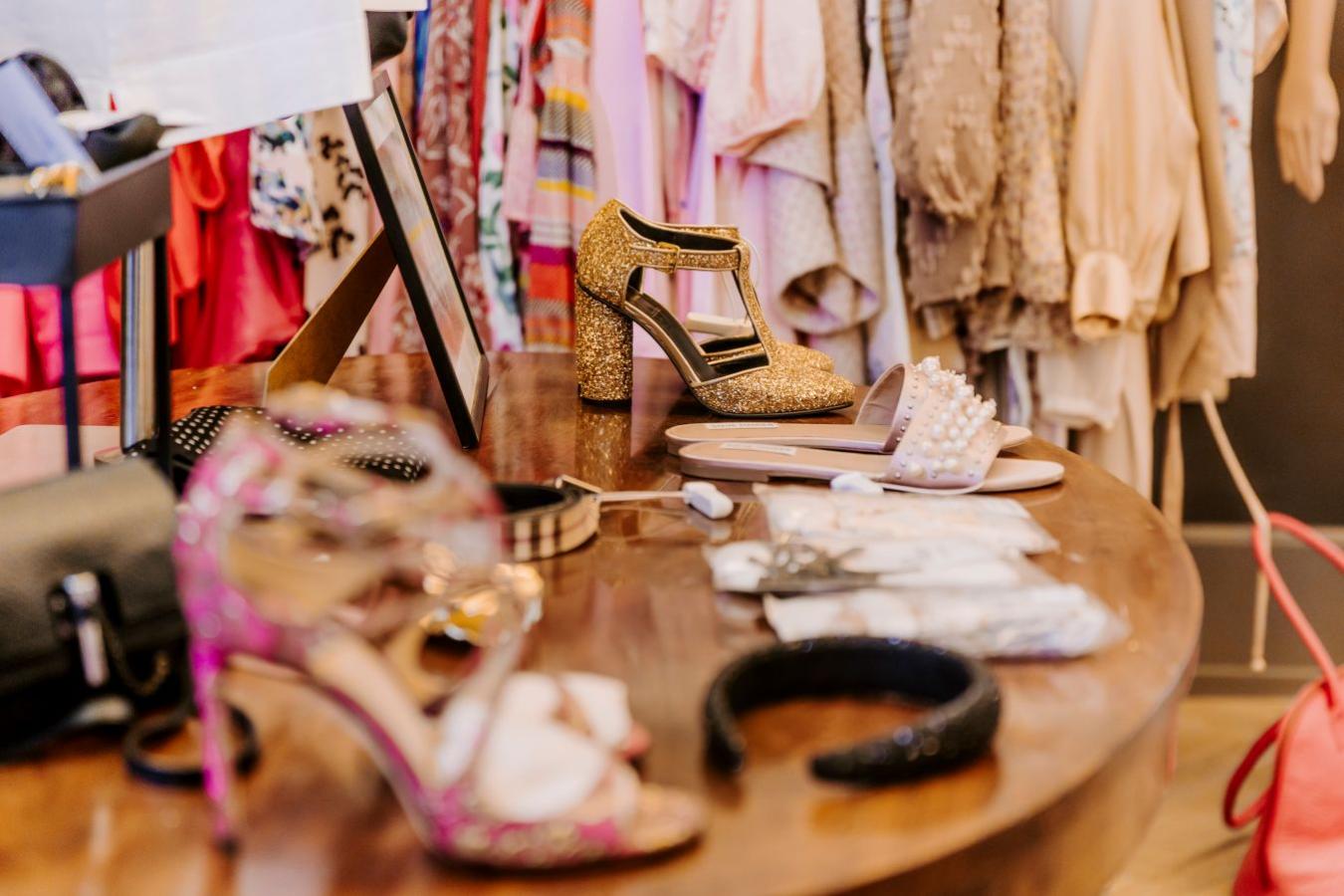 På billedet ses butikken Re-love i Middelfart. I forgrunden er et bord med tilbehør, sko og smykke. Man fornemmer luksus og nøje udvalgt genbrug. I baggrunden er et tøjstativ med kjole i forskellige farver, med perler, blonder og og pufærmer.