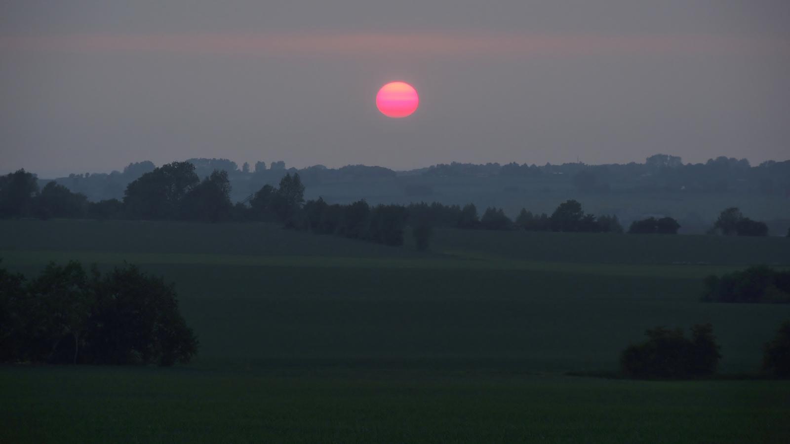Båring Banke ses om aftenen. Solen, der er helt lyserød, er ved at gå ned. Man kan stadig skimte markerne og træerne, men om lidt er det hele mørkt