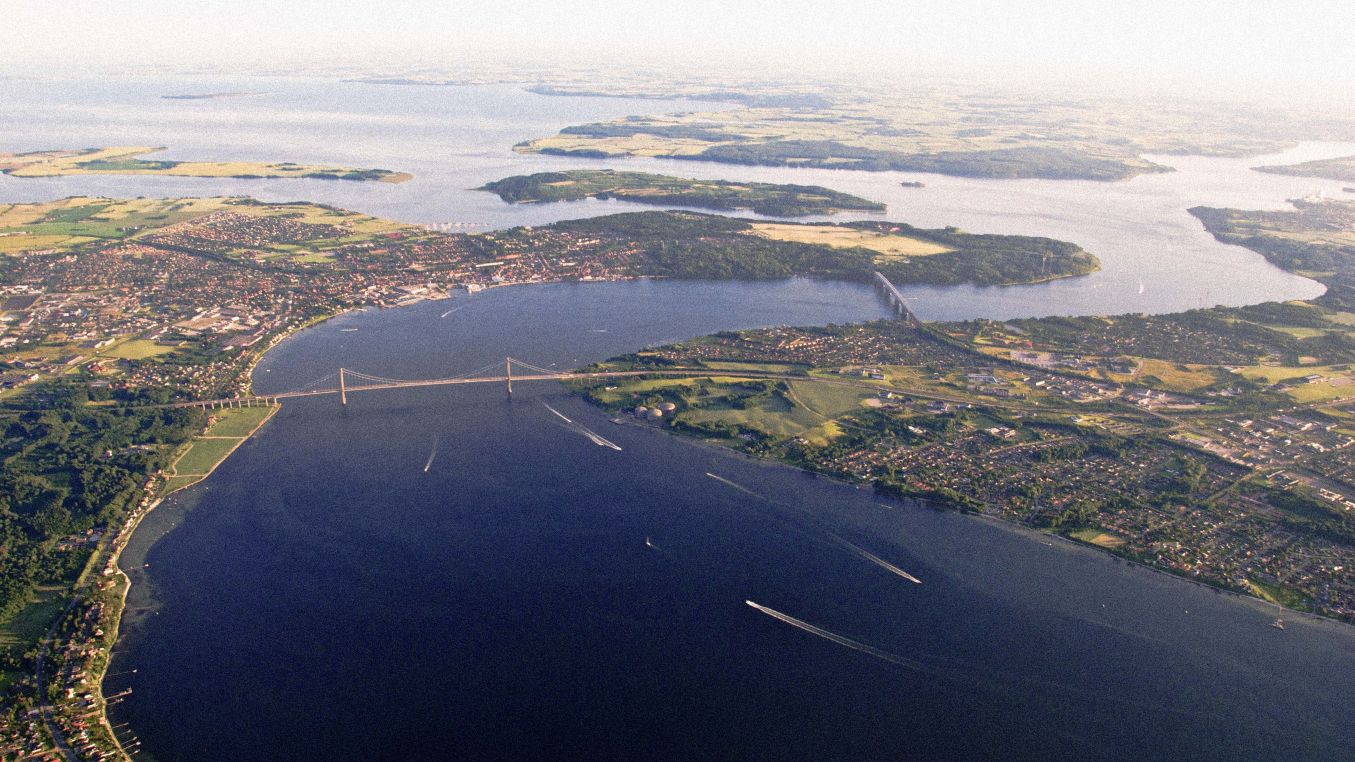 Middelfart og Lillebælt set oppefra med et dronekamera. På billedet ser man hvordan den nye og gamle Lillebæltsbro forbinder Fyn og Jylland. Det er en sommerdag, himlen er blå og naturen er grøn.
