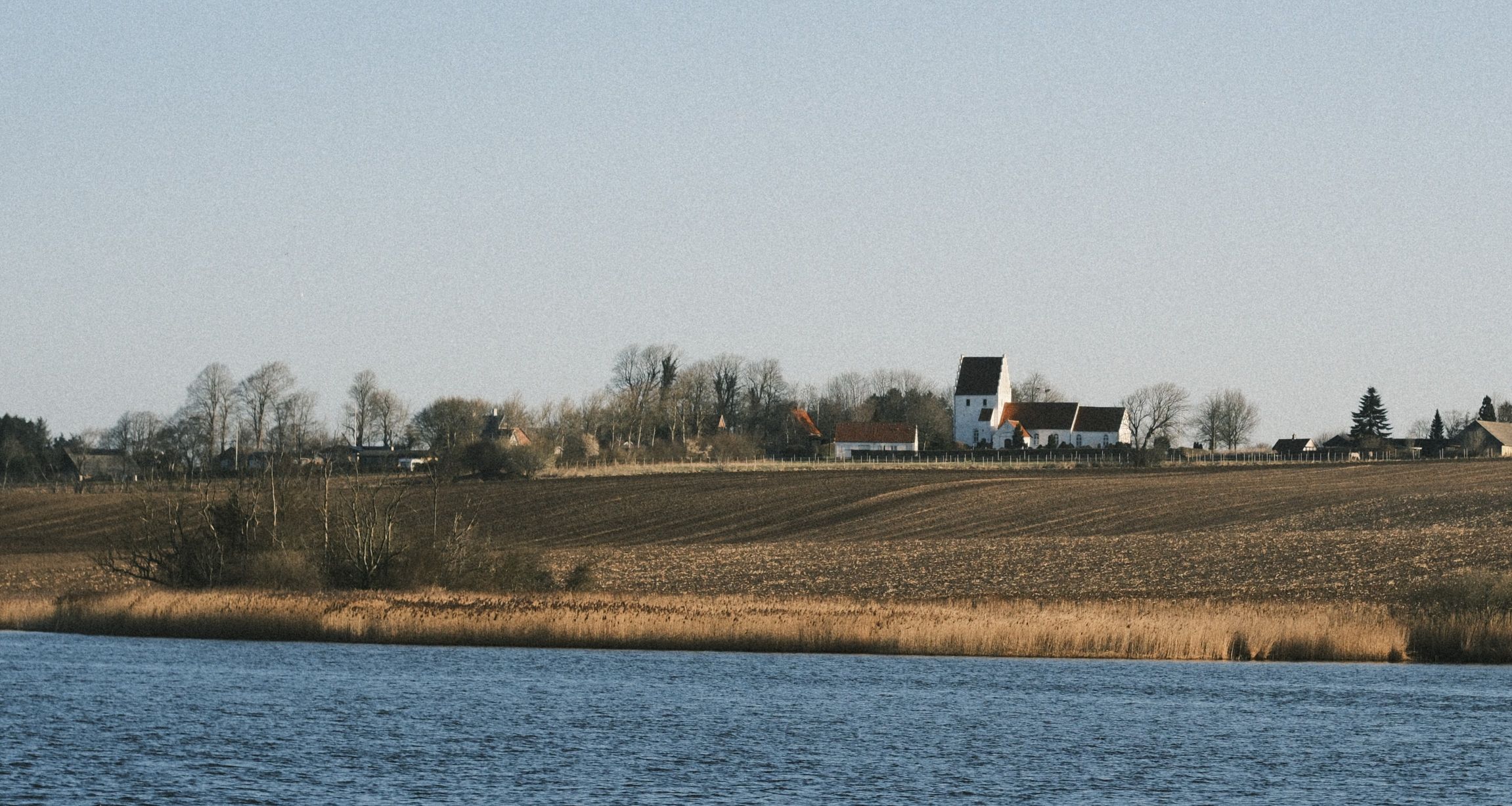 Fønsvang sø i forgrunden, bagved ligger en mark og på toppen Føns Kirke