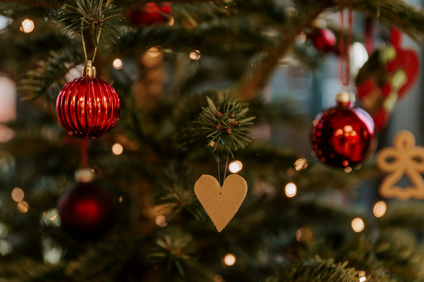 To røde julekugler og et keramik hjerte hænger på et juletræ med ls i. 